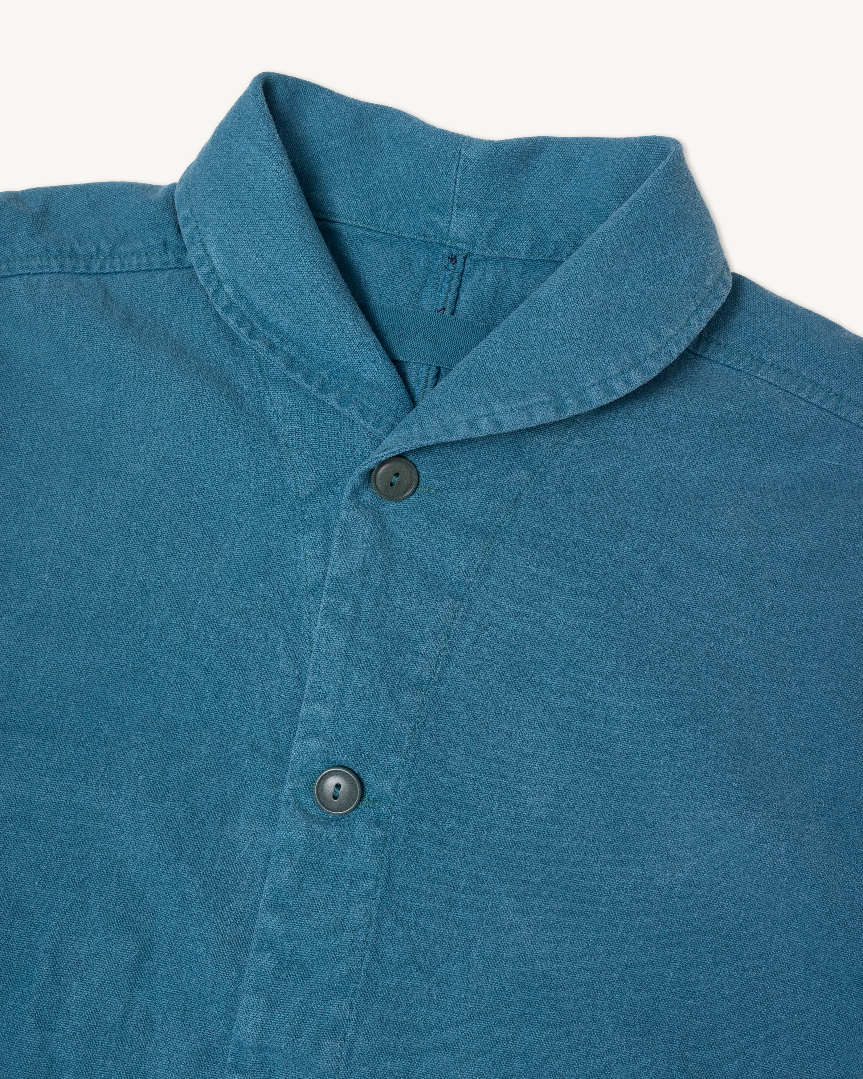 Close-up of a blue shirt collar with buttons on a white background. Shepherds Shirt in Barracuda Blue Double Dipped Hemp Cloth.