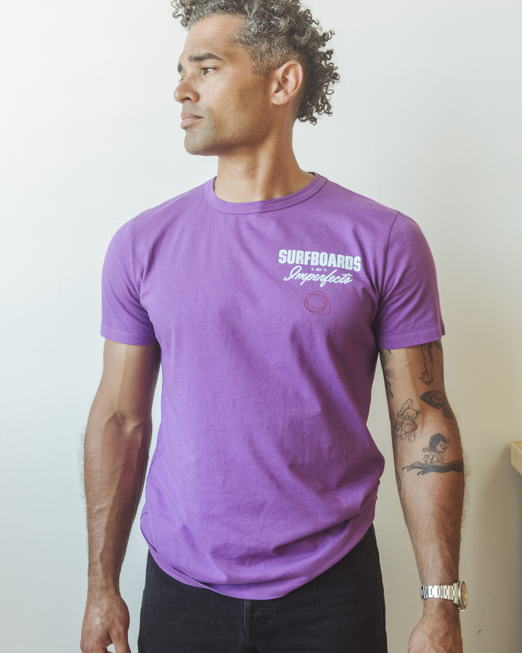 Men’s purple graphic t-shirt made from organic cotton, featuring “Surfboards by Imperfects” chest print and circular hand-drawn logo, styled with black pants.
Magic Carpet T-Shirt in Purple Magic.
