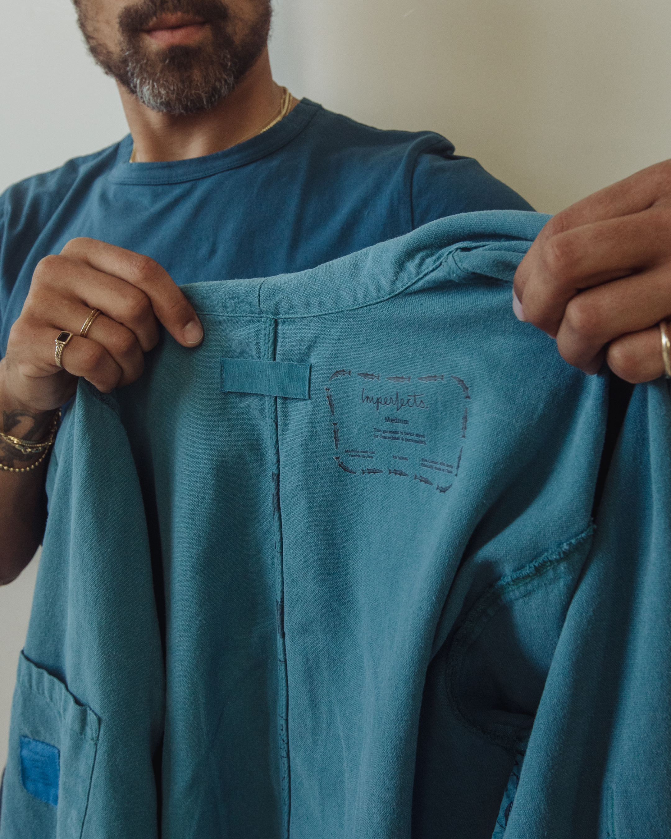 Person holding a blue jacket with a brand logo on a neutral background. Shepherds Shirt in Barracuda Blue Double Dipped Hemp Cloth.